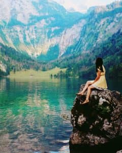 Foto de uma mulher sentada em uma rocha com uma paisagem com montanhas e lago ao fundo com o resultado final da edição