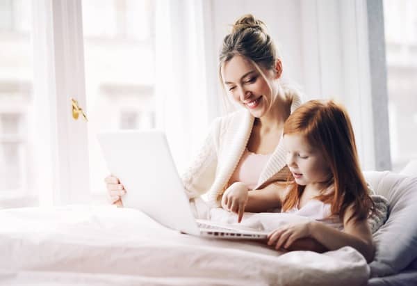 Mamá con su hija en la cama jugando con una computadora. La foto ha sido editada con filtros de AirBrush.