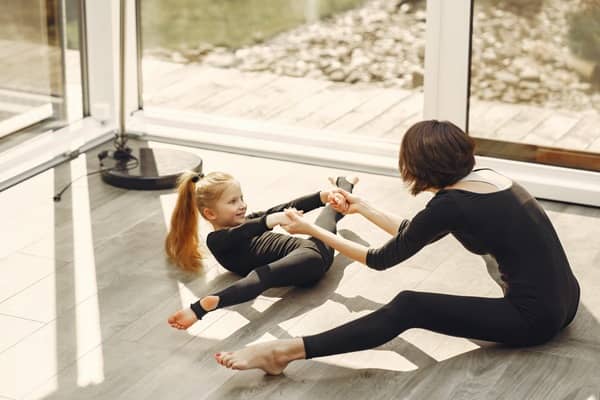 Foto de mamá practicando ballet o gimnasia con su hija. Ambas están vestidas con un payasito negro y están haciendo estiramientos.