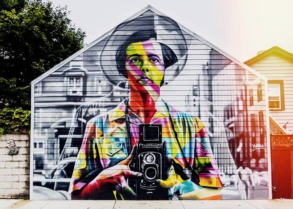 Arte urbano de un hombre sosteniendo una cámara, pintado en la fachada de una casa.