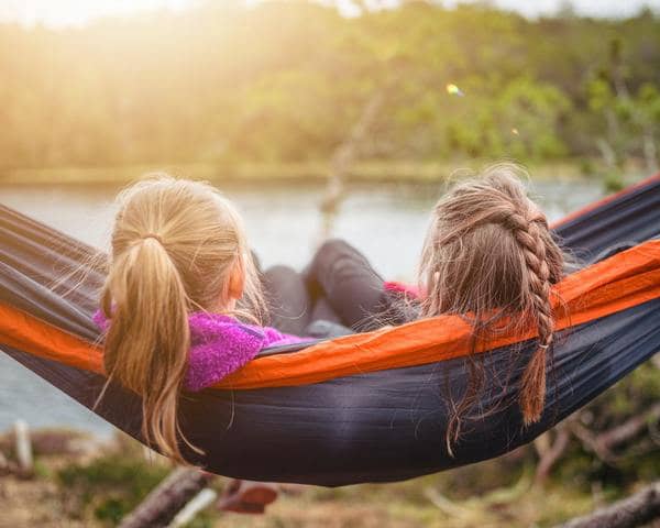 two women in a hammock facing a lake