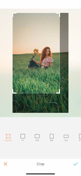 Picture of a ginger woman holding yellow flowers sitting in grass at the open field being edited by AirBrush with the Crop Tool