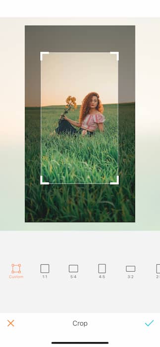 Picture of a ginger woman holding yellow flowers sitting in grass at the open field being edited by AirBrush with the Crop Tool