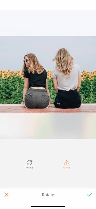 Picture of two girl friends sitting and looking at a sunflower field being edited by AirBrush with the Rotate Tool