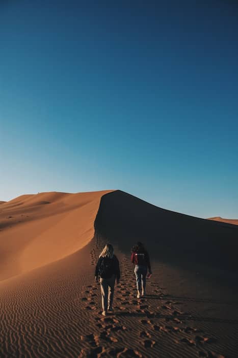 two women walking on a sand dune