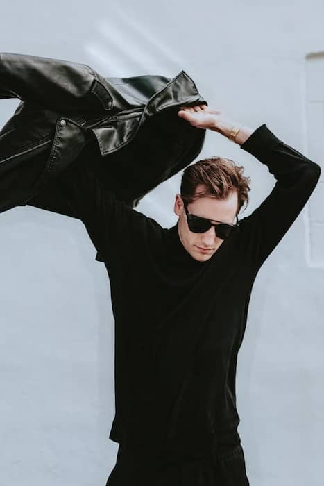 man dressed in all black putting on a leather jacket