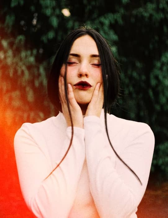 woman wearing a white top holds her face in her hands