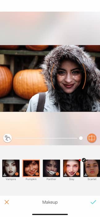 smiling woman wearing hooded jacket stands in front of pumpkins