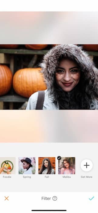 smiling woman wearing hooded jacket stands in front of pumpkins