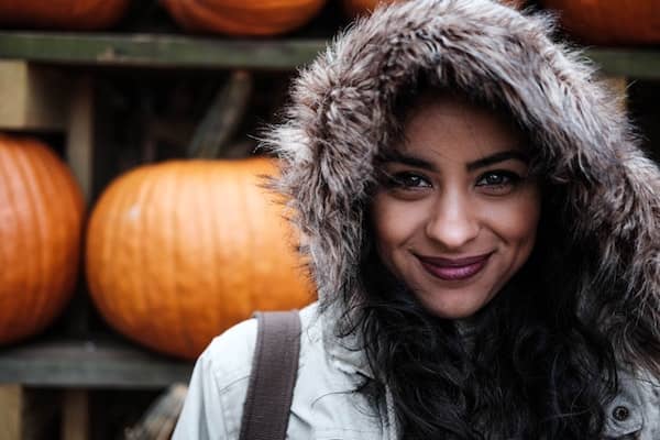 smiling woman wearing hooded jacket stands in front of pumpkins