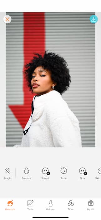 woman wearing a white jacket stands in front of white wall with a red arrow