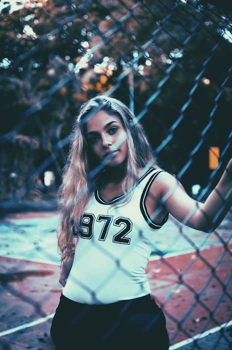 woman in white tank top standing against chainlink fence