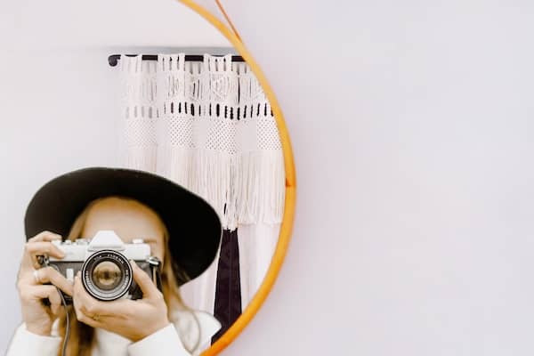 woman wearing a black hat takes a photo with a vintage camera