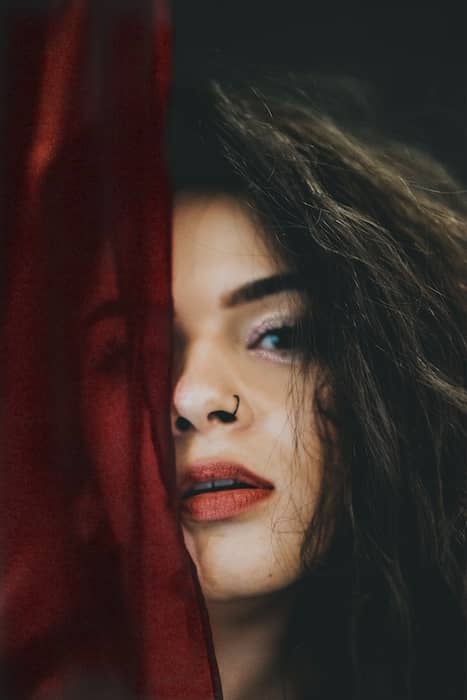 closeup photo of a woman with dark hair and nose ring, half her face is covered by dark cloth fabric