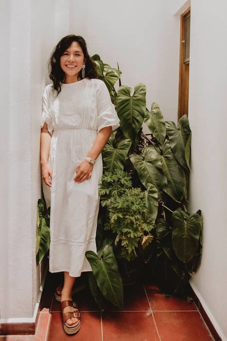  woman in a white dress standing in front of green plants