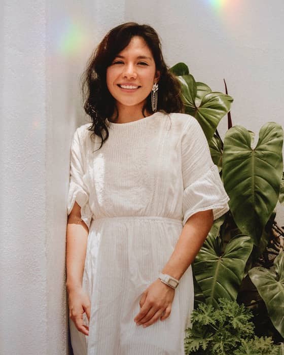  woman in a white dress standing in front of green plants