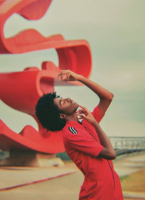 black man in red jumpsuit in front of curvy red sculpture