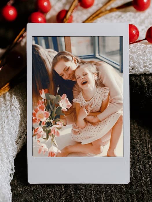 photo of mother hugging toddler daughter and laughing on an iPad with cherries background