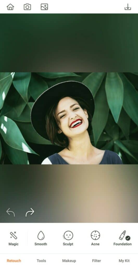 laughing woman wearing a hat in front of a leafy background