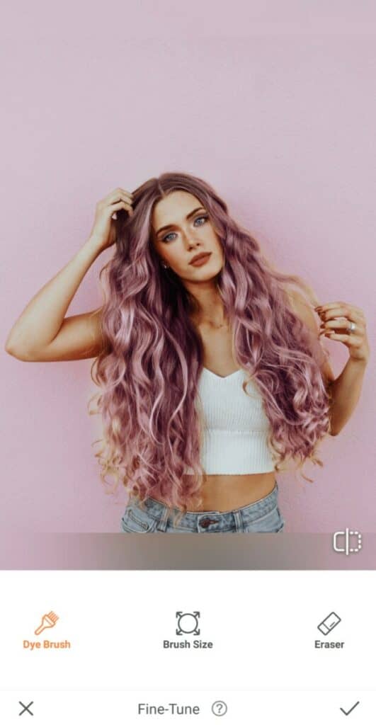 woman with purple hair in a white top stands in front of a pink wall