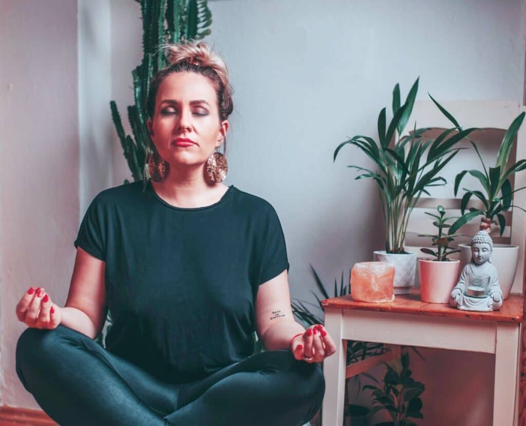 woman sitting and meditating next to plants