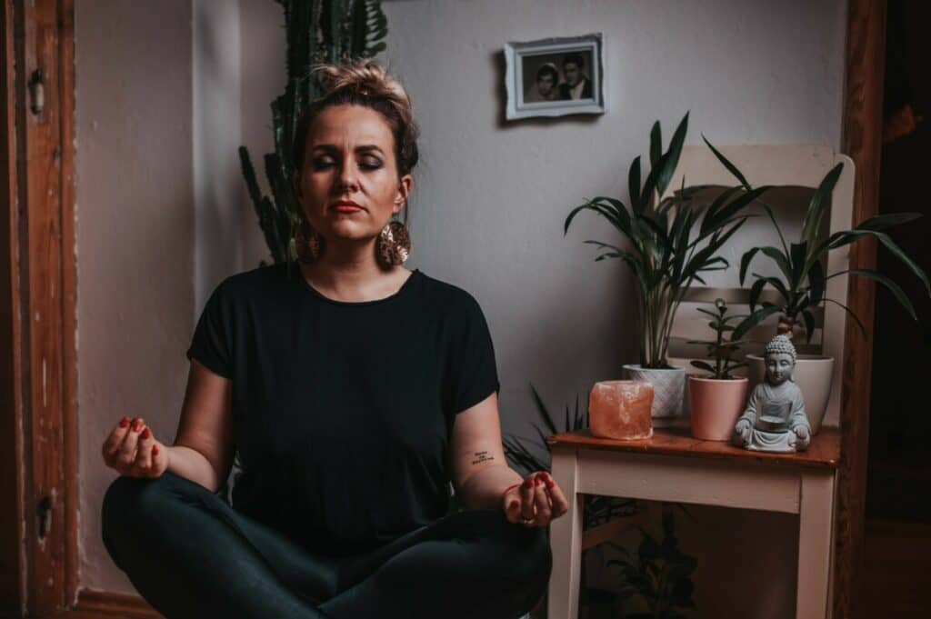 woman sitting and meditating next to plants