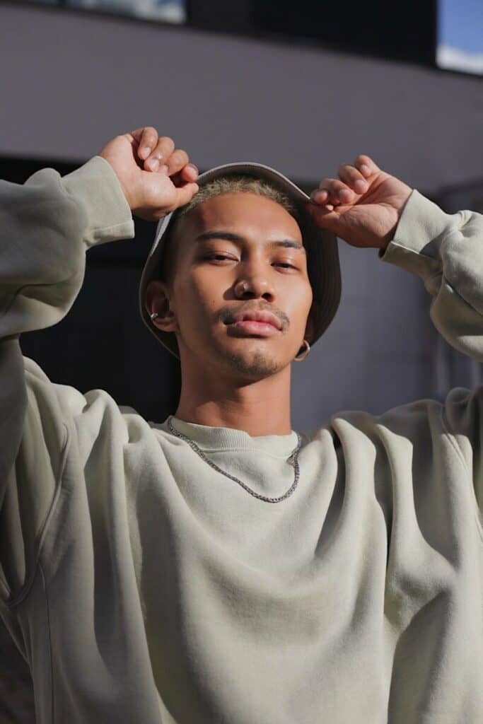 man in grey sweatshirt holding a hat on his head