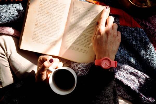 Um livro aberto no colo de uma pessoa segurando uma caneca branca de café