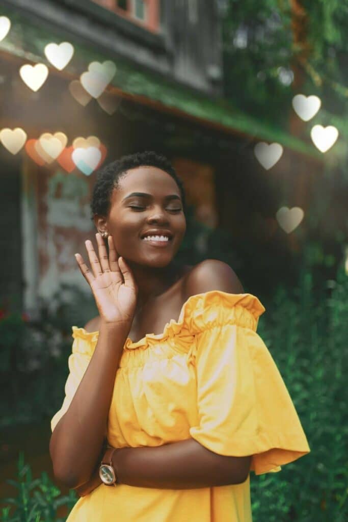 Cancer edit with smiling woman in yellow dress stands in front of background with green foliage