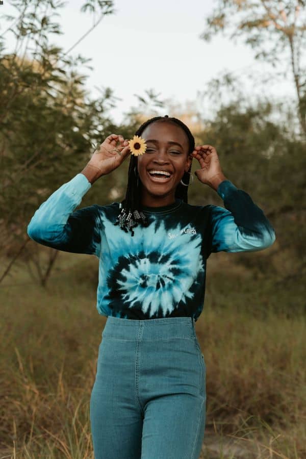 woman in tie-dyed shirt holding a sunflower outdoors