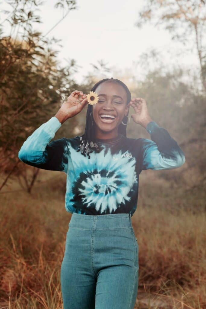 Cancer edit with woman in tie-dyed shirt holding a sunflower outdoors