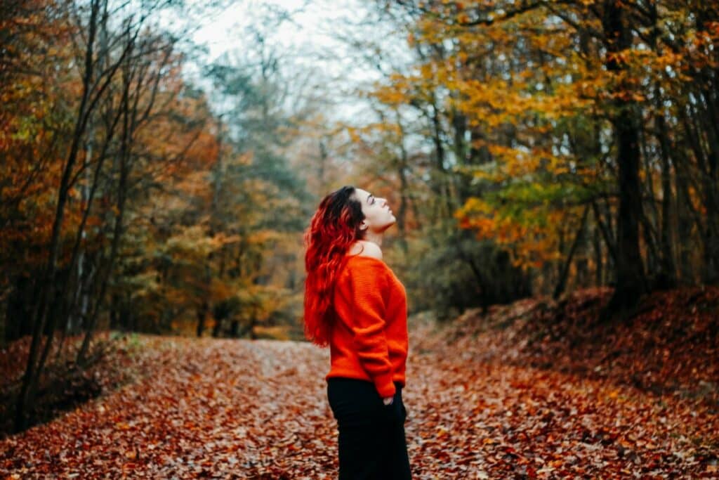 woman wearing red sweater amongst fall leaves