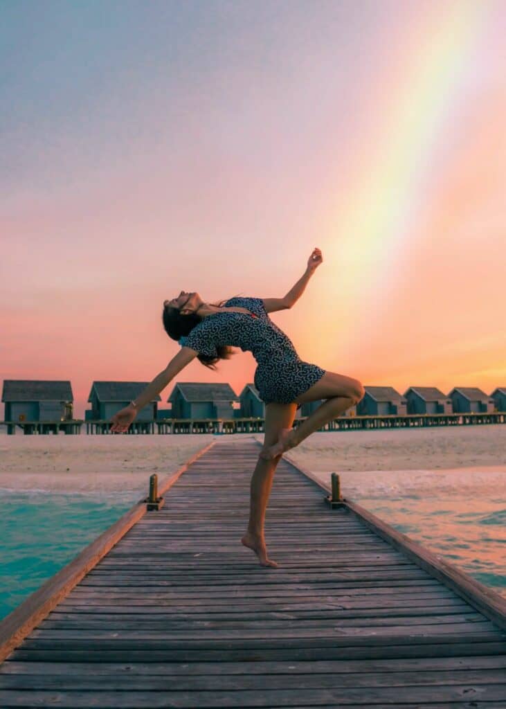 woman posing on a jetty at sunset with a rainbow in the sky